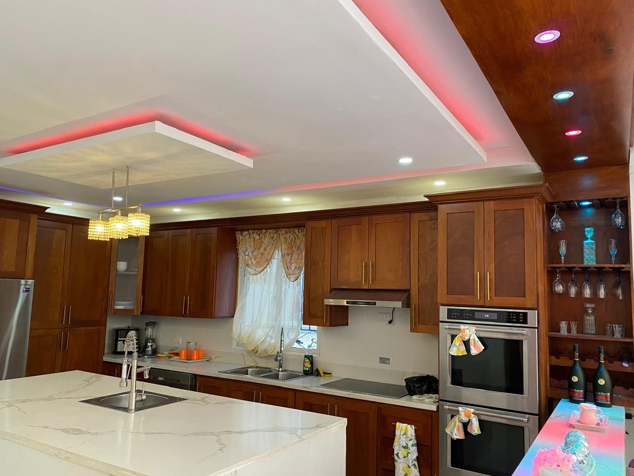 Une cuisine moderne avec des meubles en bois, un îlot en marbre, des appareils électroménagers en acier inoxydable et des luminaires suspendus.