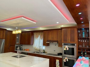 A modern kitchen with wooden cabinets, a marble island, stainless steel appliances, and pendant lighting.