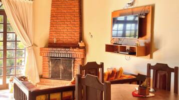 Un comedor con chimenea de ladrillo, sillas de madera y un televisor montado en la pared.
