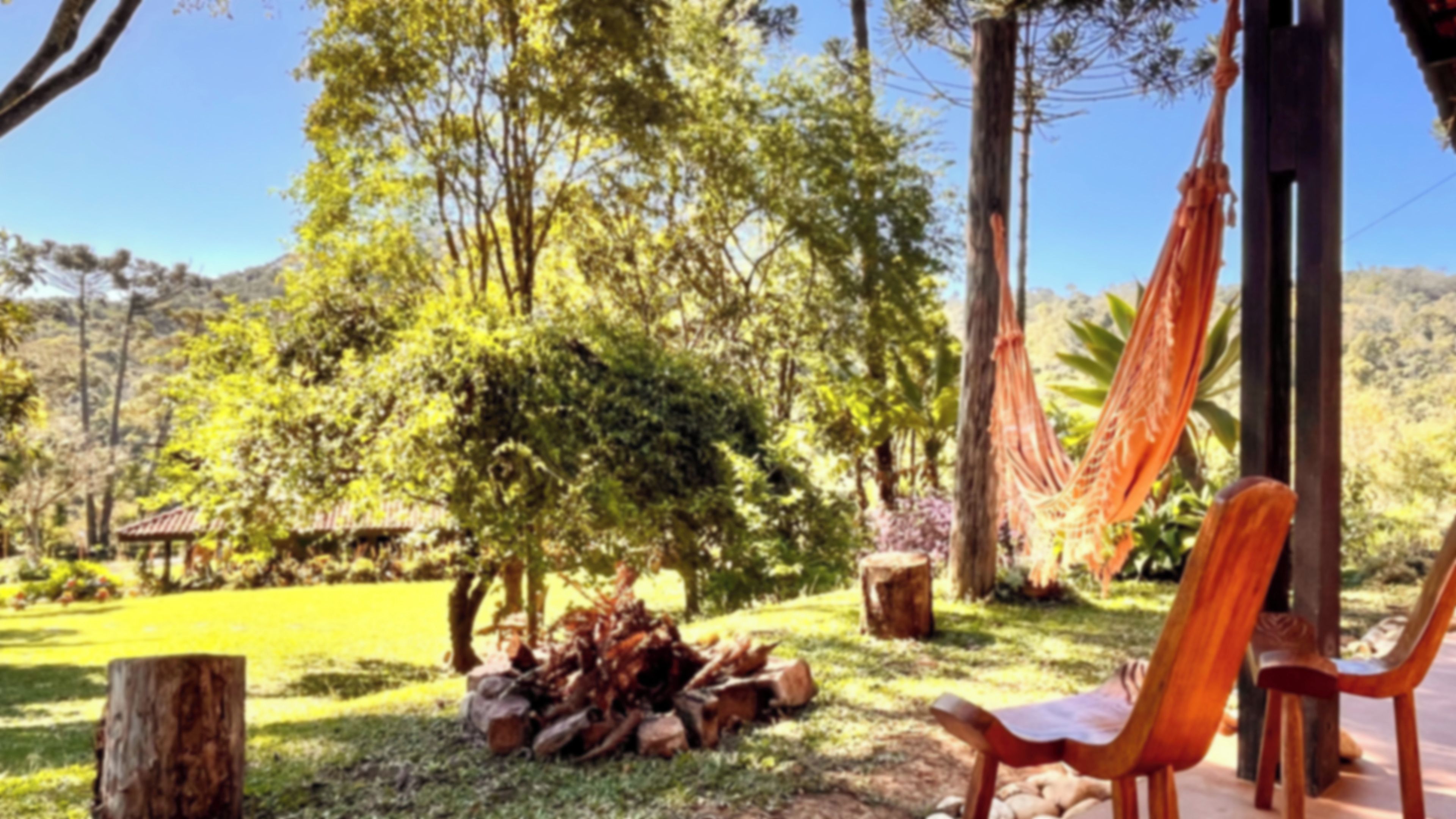 Una hamaca, una silla de madera y una pila de troncos en un jardín.