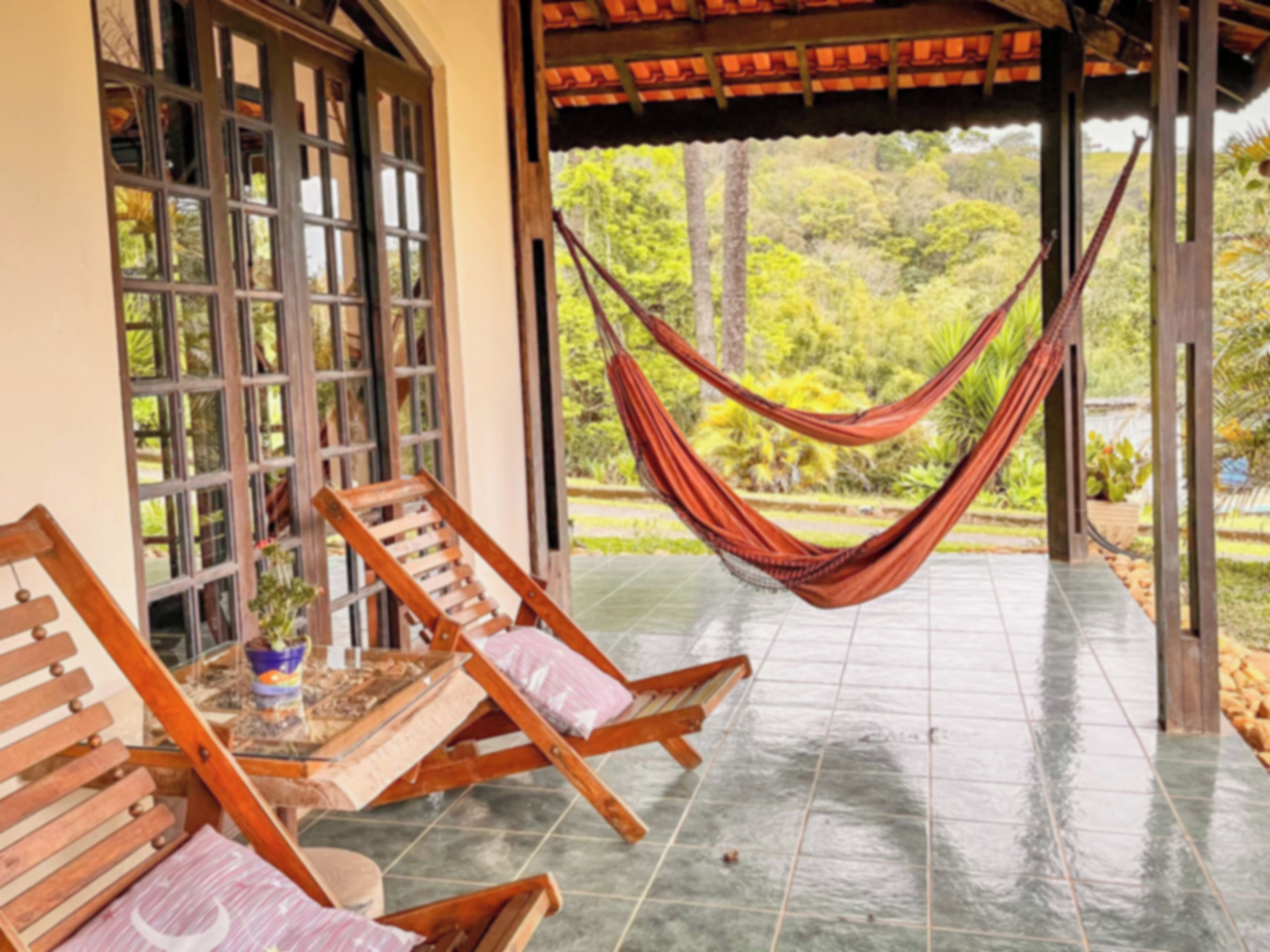 A covered outdoor seating area with wooden chairs and a hammock, overlooking a lush garden.