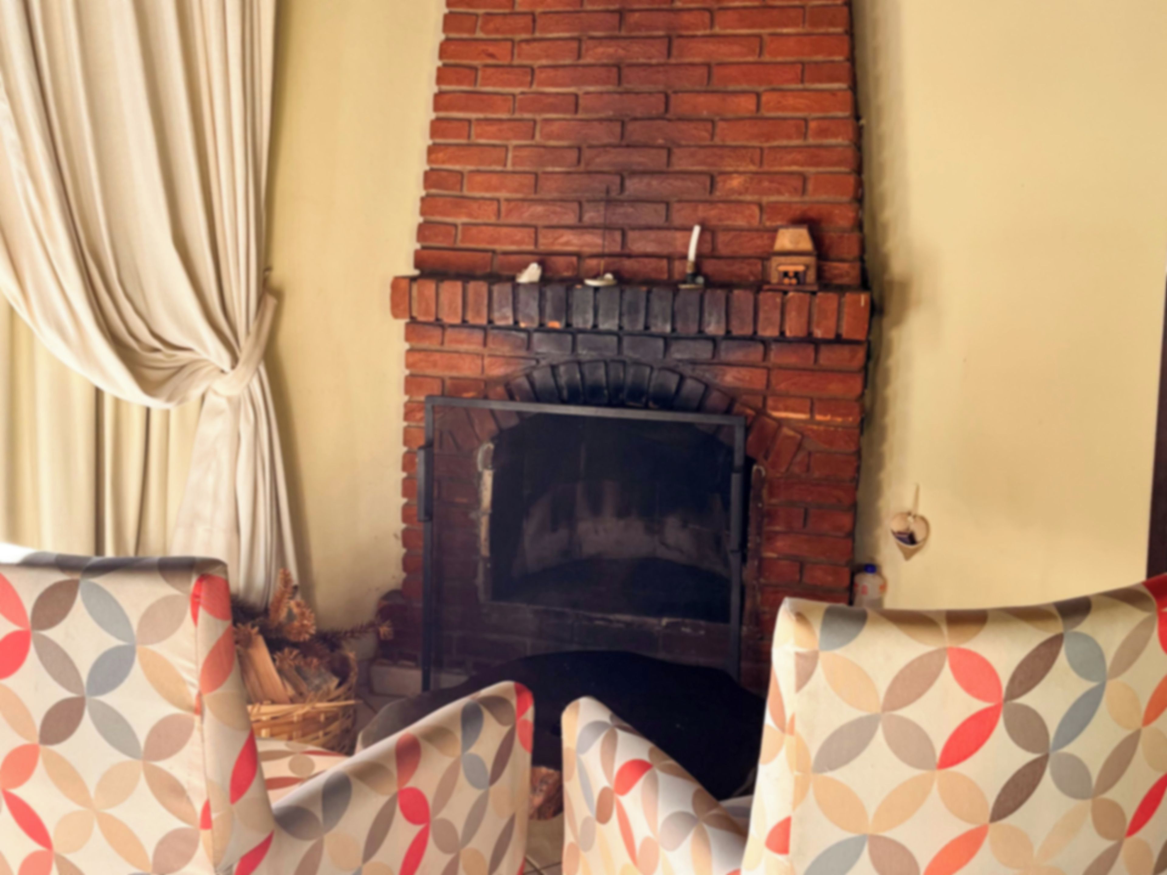 A room with a brick fireplace, patterned chairs, and a curtain.
