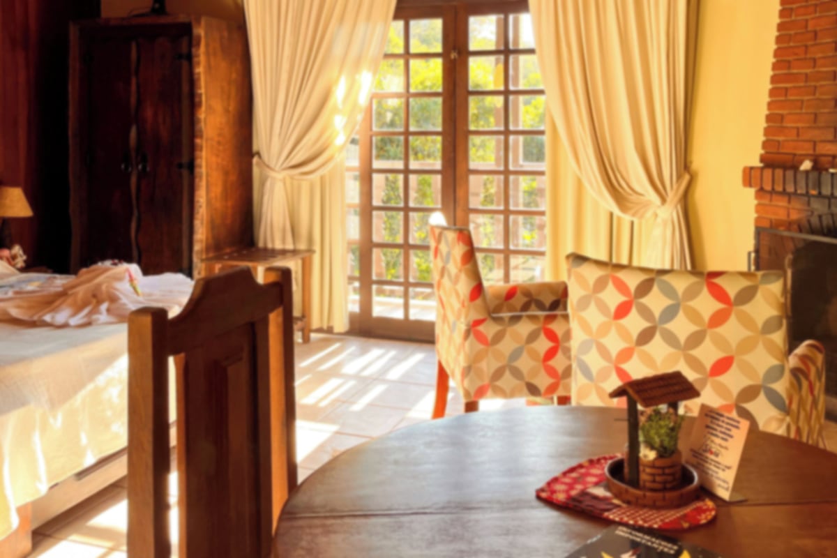 A room with a bed, a wooden chair, a table with a placemat, and a fireplace.