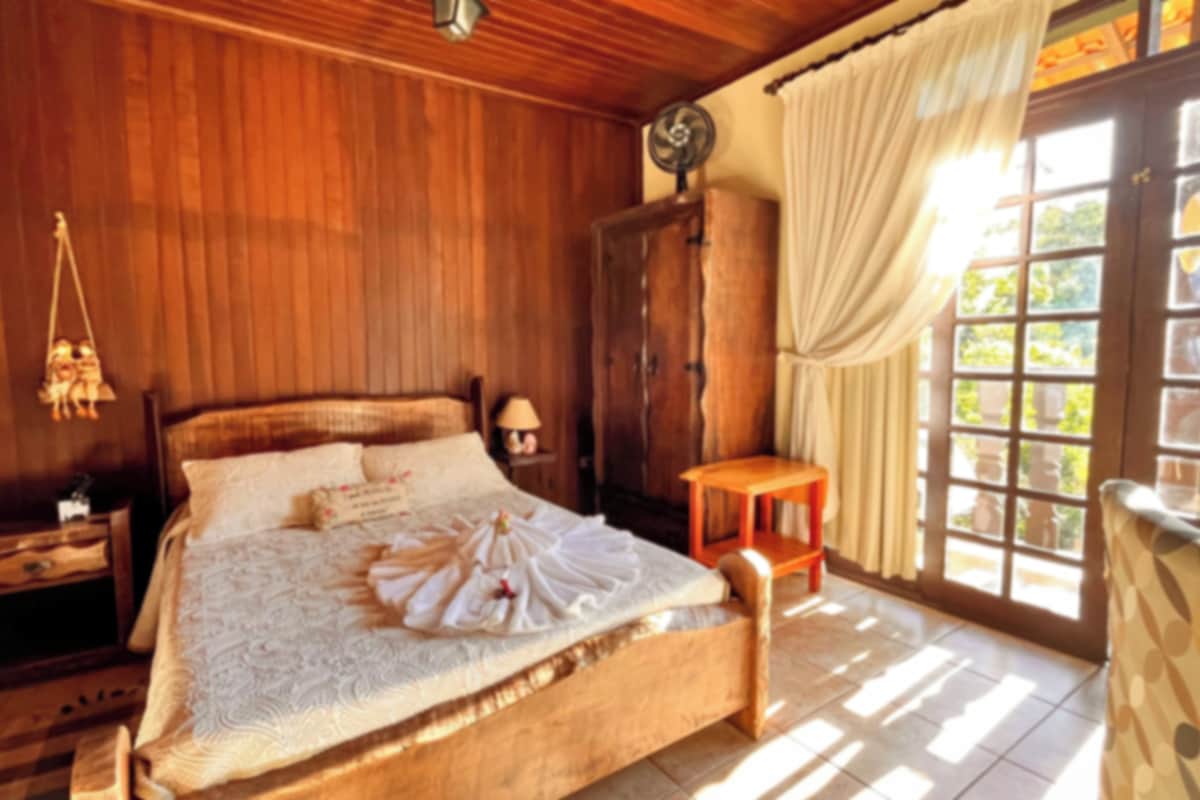 A wooden bedroom with a bed, nightstands, a wooden wardrobe, and a window with curtains.