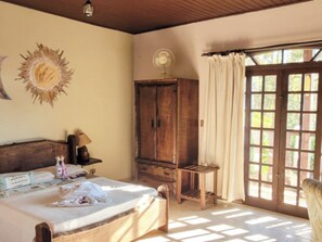 A bedroom with a bed, a wooden cabinet, a small table, a fan, and a window with curtains.
