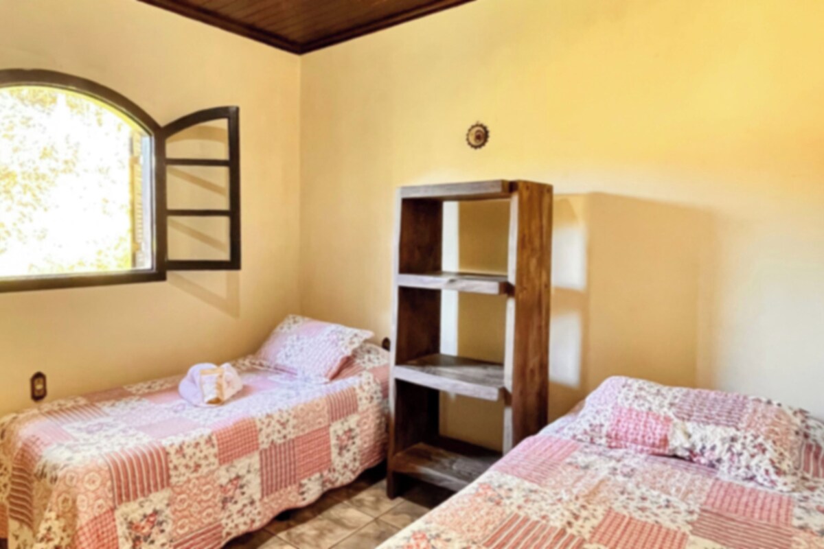 A room with two beds, a window with a view, and a wooden shelf unit.
