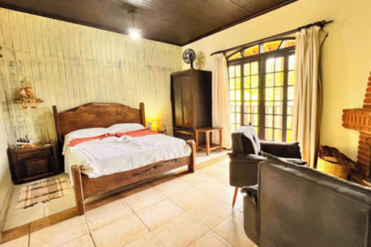 A bedroom with a wooden bed, a television, a brick fireplace, and a window with curtains.