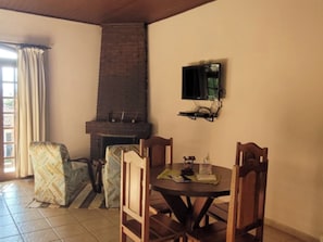 A dining area with a brick fireplace, a television mounted on the wall, and a patterned armchair. - VELINN Pousada Lua e Sol (Santo Antônio do Pinhal)