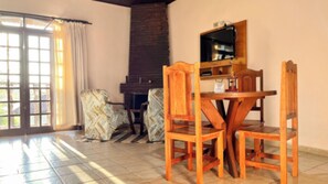A dining area with a wooden table and chairs, a fireplace, and a view through a glass door. - VELINN Pousada Lua e Sol (Santo Antônio do Pinhal)