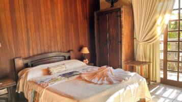 A bedroom with a wooden headboard, a bed with a floral bedspread, a nightstand with a lamp, and a wooden wardrobe.