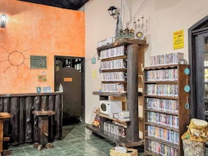 A library with bookshelves, a welcome sign, and a sun decoration on the wall. - VELINN Pousada Lua e Sol (Santo Antônio do Pinhal)