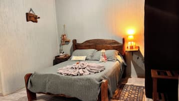 A bedroom with a wooden bed, a bedside table with a lamp, and a wall-mounted shelf.
