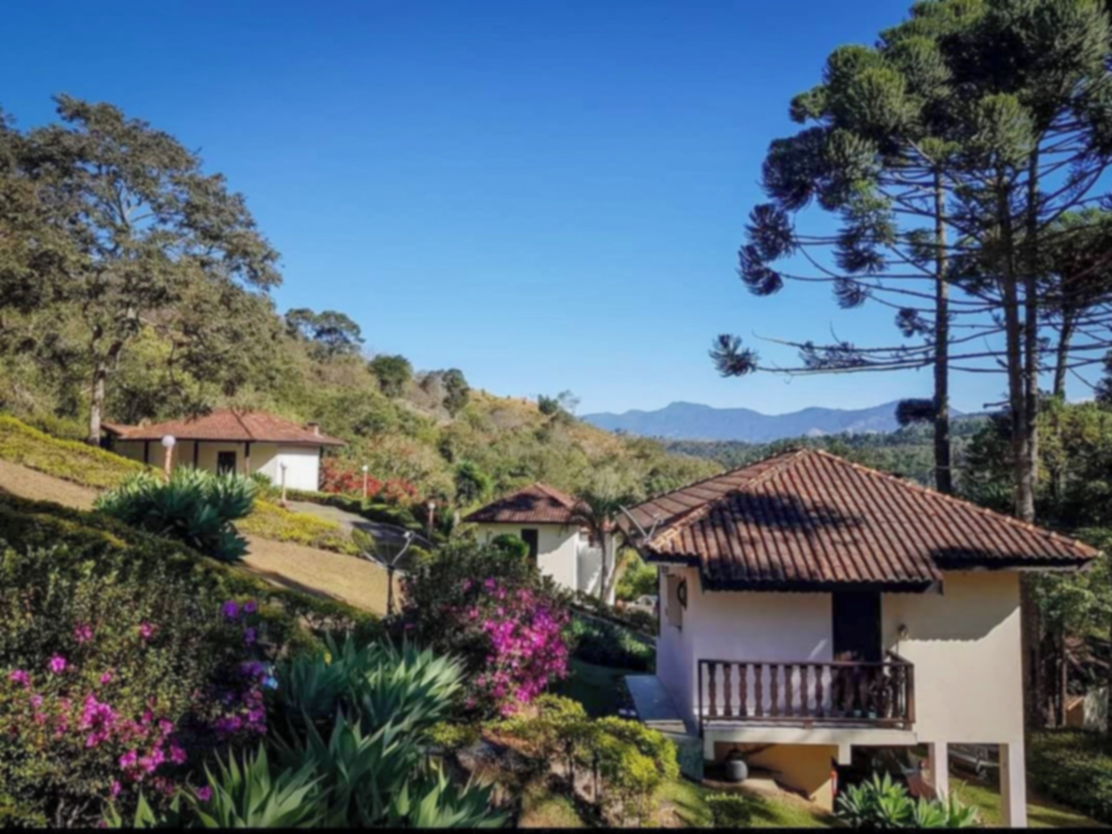 Una propiedad en una ladera con varias construcciones, incluyendo una casa con balcón y una estructura más pequeña con techo de tejas.