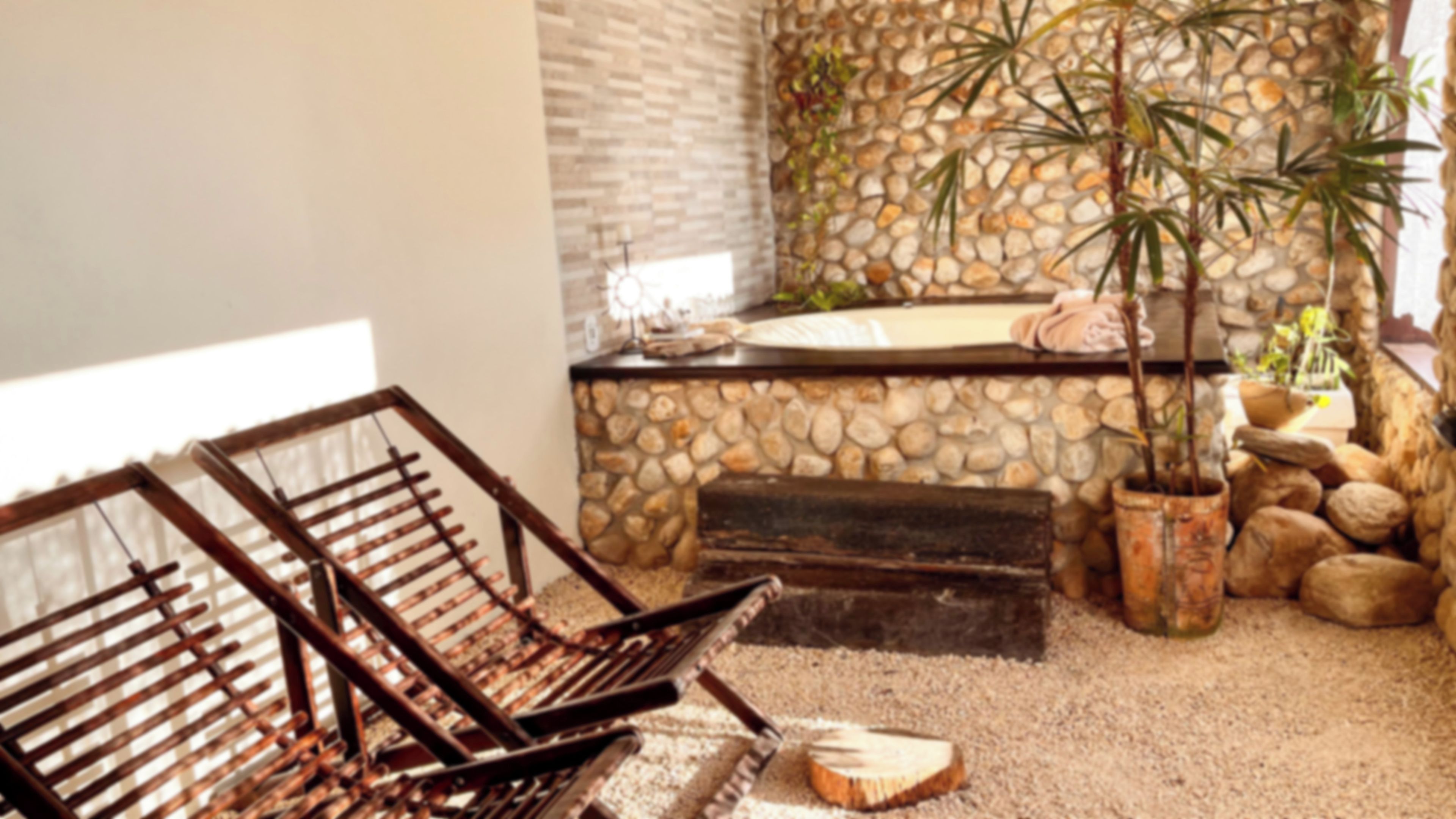 Quarto com parede de pedra, um banco de madeira, uma banheira e um vaso de planta.