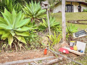 Un espace jardin agrémenté de grandes plantes vertes, d’un panneau en bois avec une inscription et d’une nichoir.