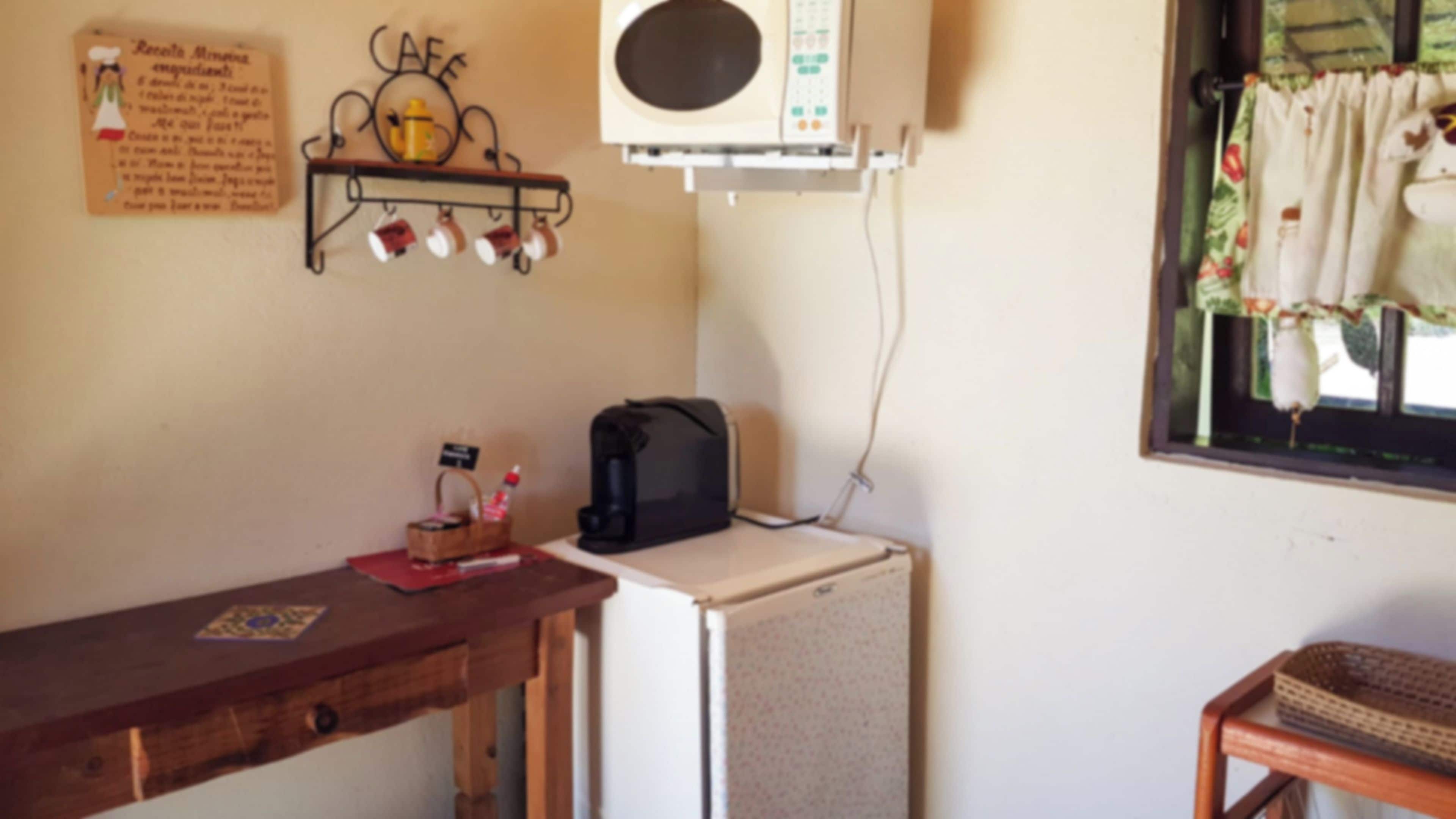 Una kitchenette compacta con microondas, un refrigerador pequeño, una cafetera y una estantería con tazas.