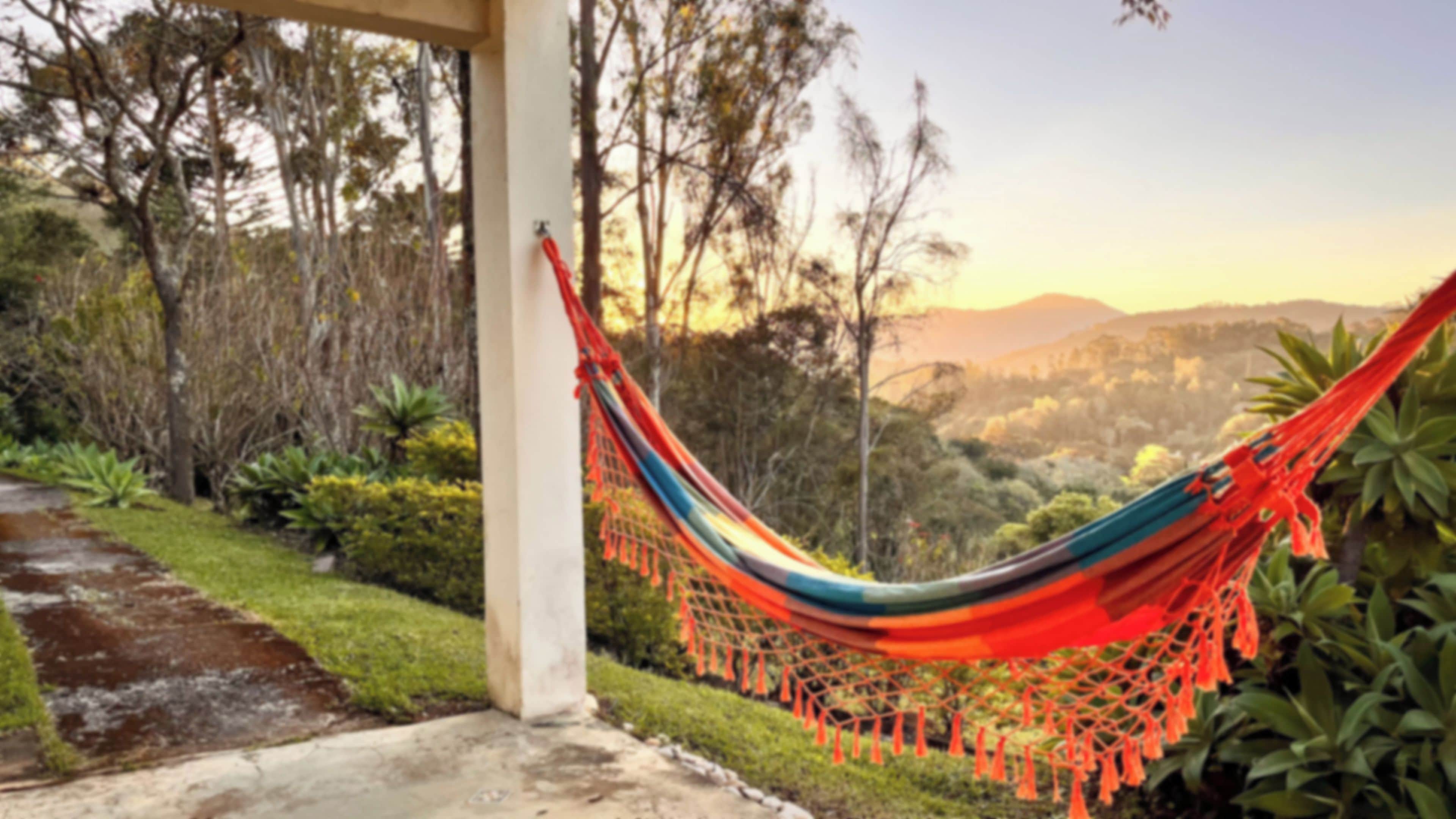 A hammock tied to a concrete pillar, overlooking a landscaped garden with various plants and a mountainous backdrop.