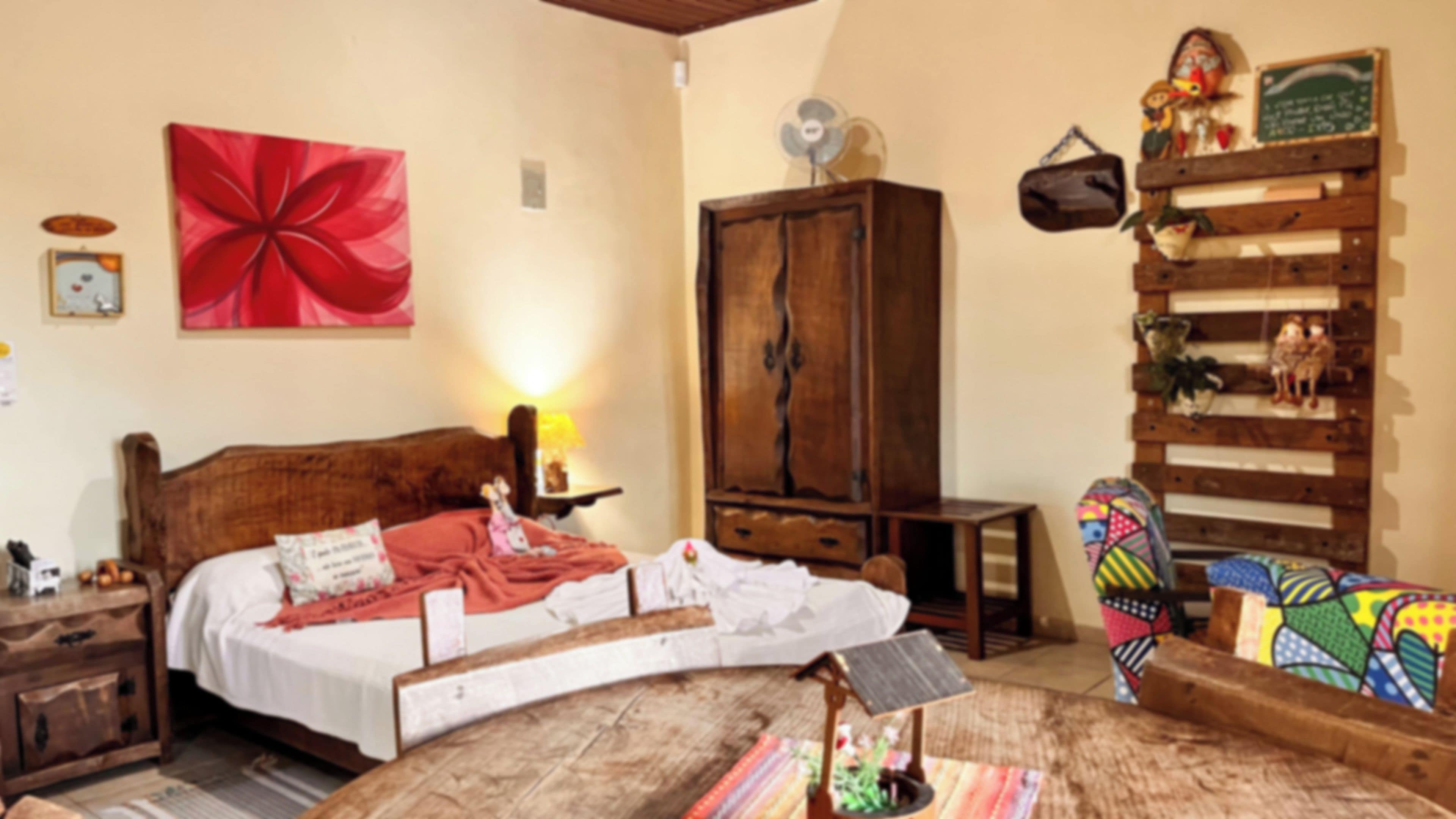 A bedroom with a bed, a wooden wardrobe, a colorful sofa, and a wall with a large red flower painting.