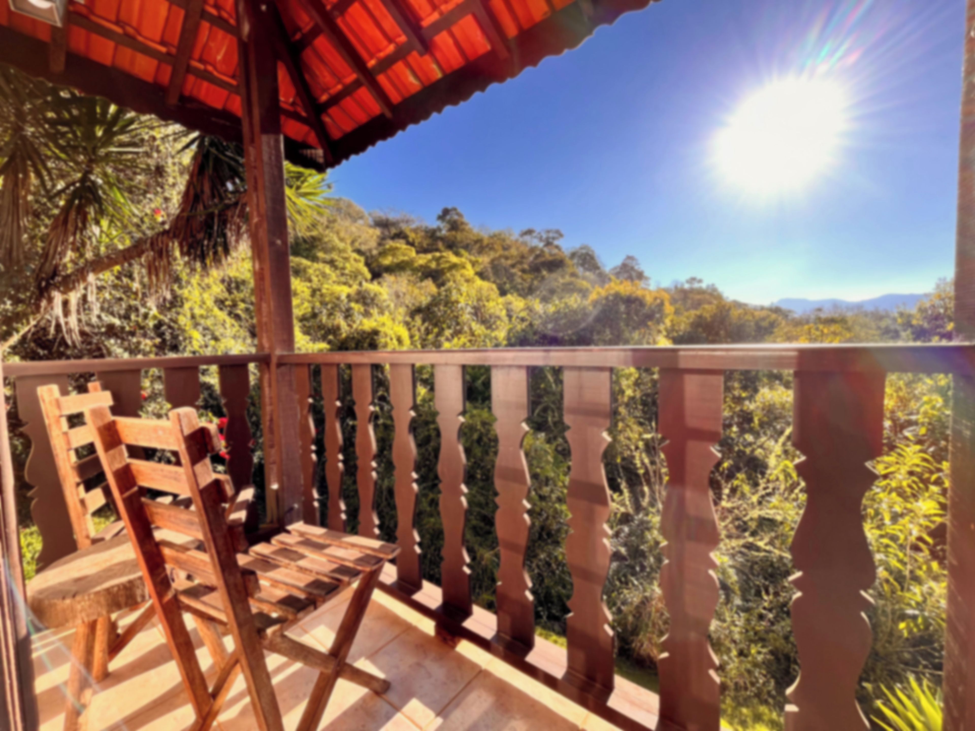 Una terraza de madera con barandilla, una silla de madera y vistas a un paisaje boscoso.