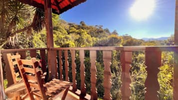 Una terraza de madera con barandilla, una silla de madera y vistas a un paisaje boscoso.