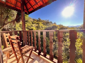 A wooden deck with a railing, a wooden chair, and a view of a forested landscape.