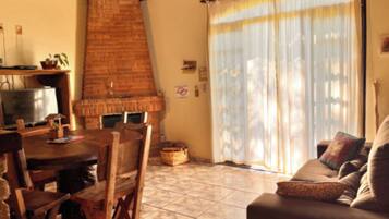 A living room with a brick fireplace, a television, a sofa, and a dining table with chairs.