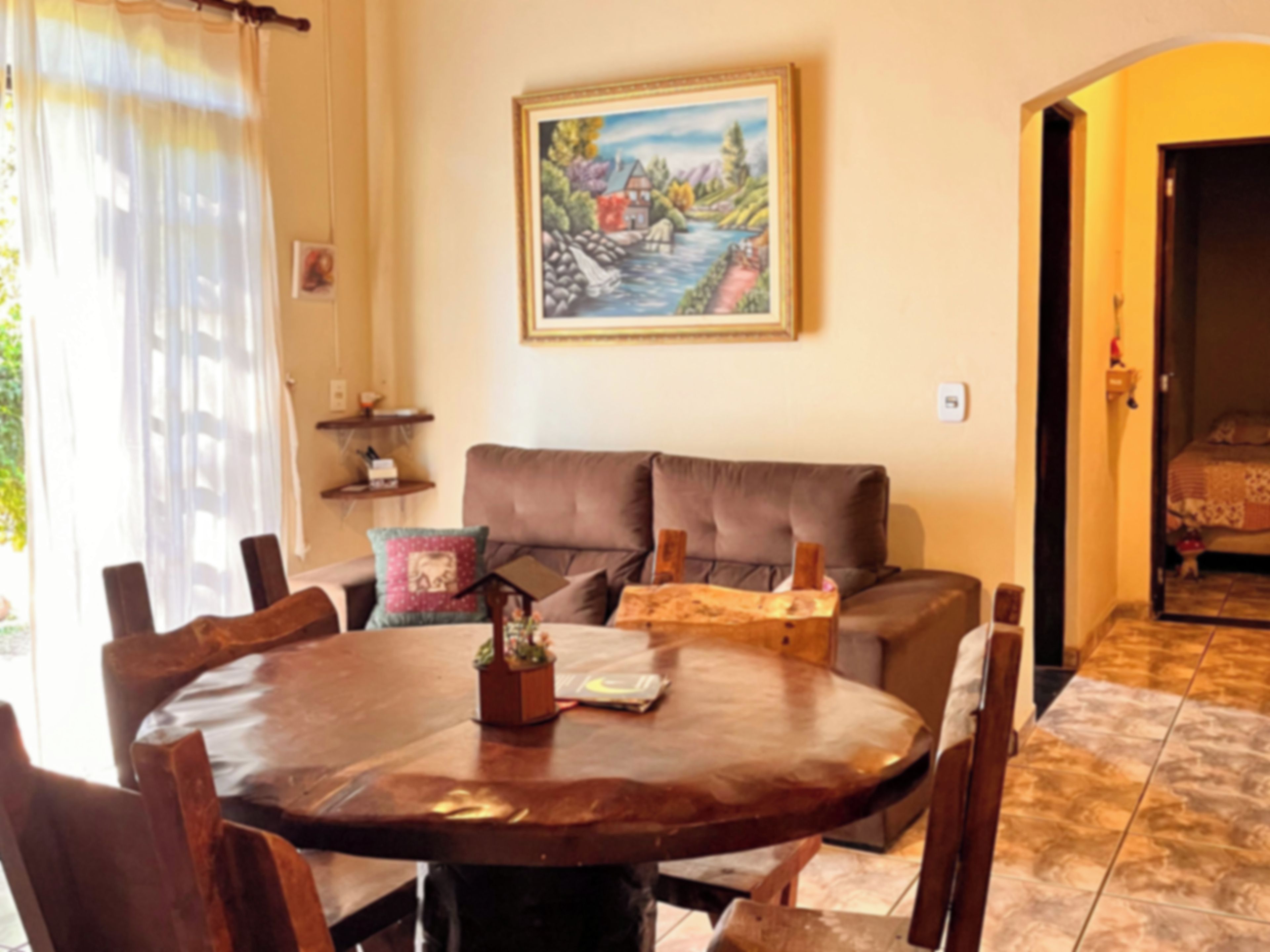A dining area with a round wooden table, chairs, a sofa, and a painting on the wall.