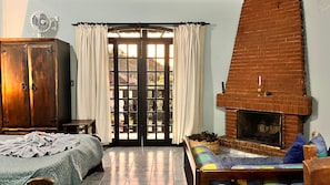 A room with a bed, a wooden wardrobe, a fireplace, and a large window with curtains.