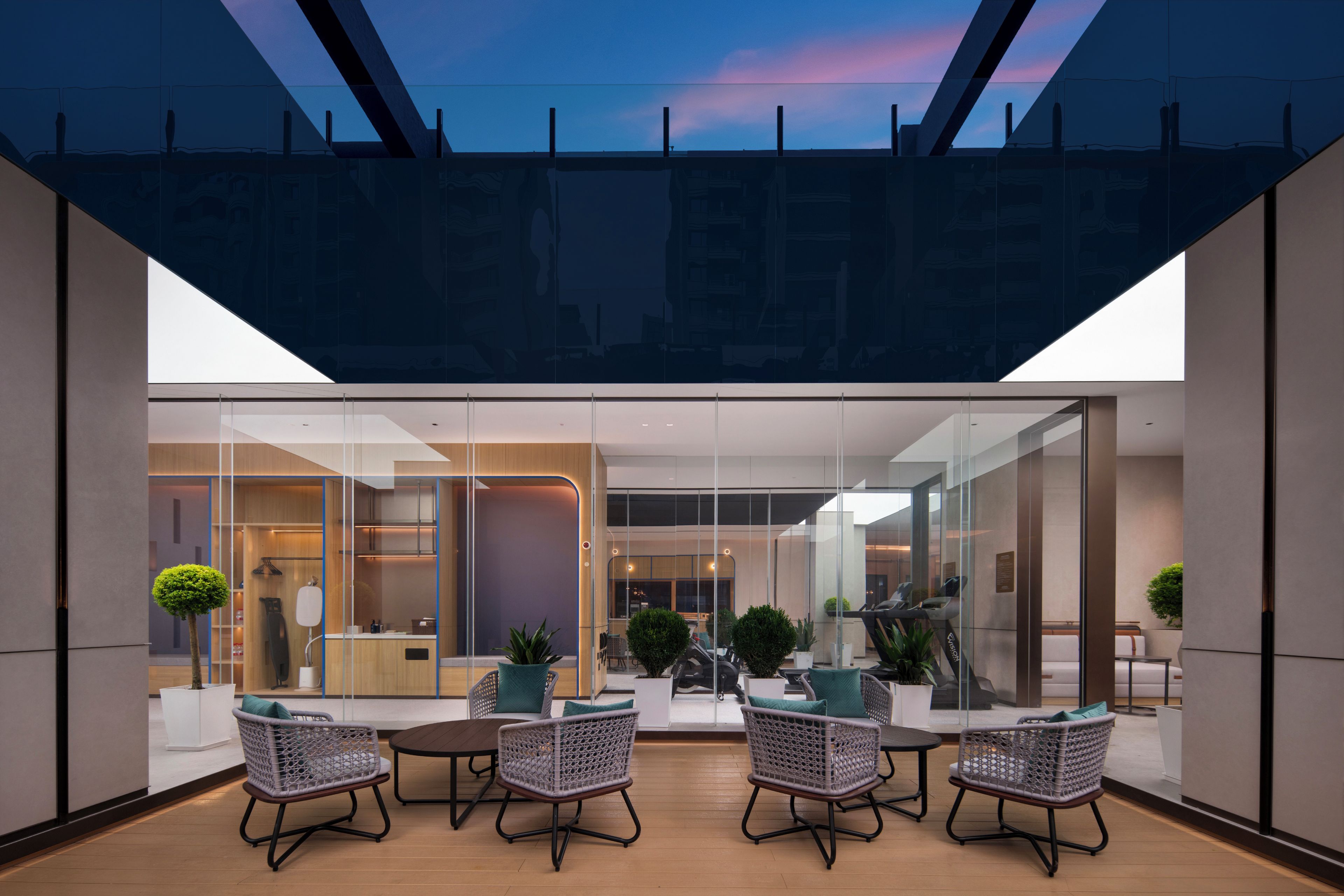 A modern outdoor seating area with wicker chairs and a table, overlooking a glass-enclosed interior space.