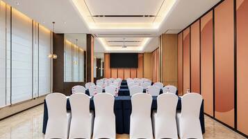 A conference room with rows of white chairs, a long table, and a projector screen at the front.
