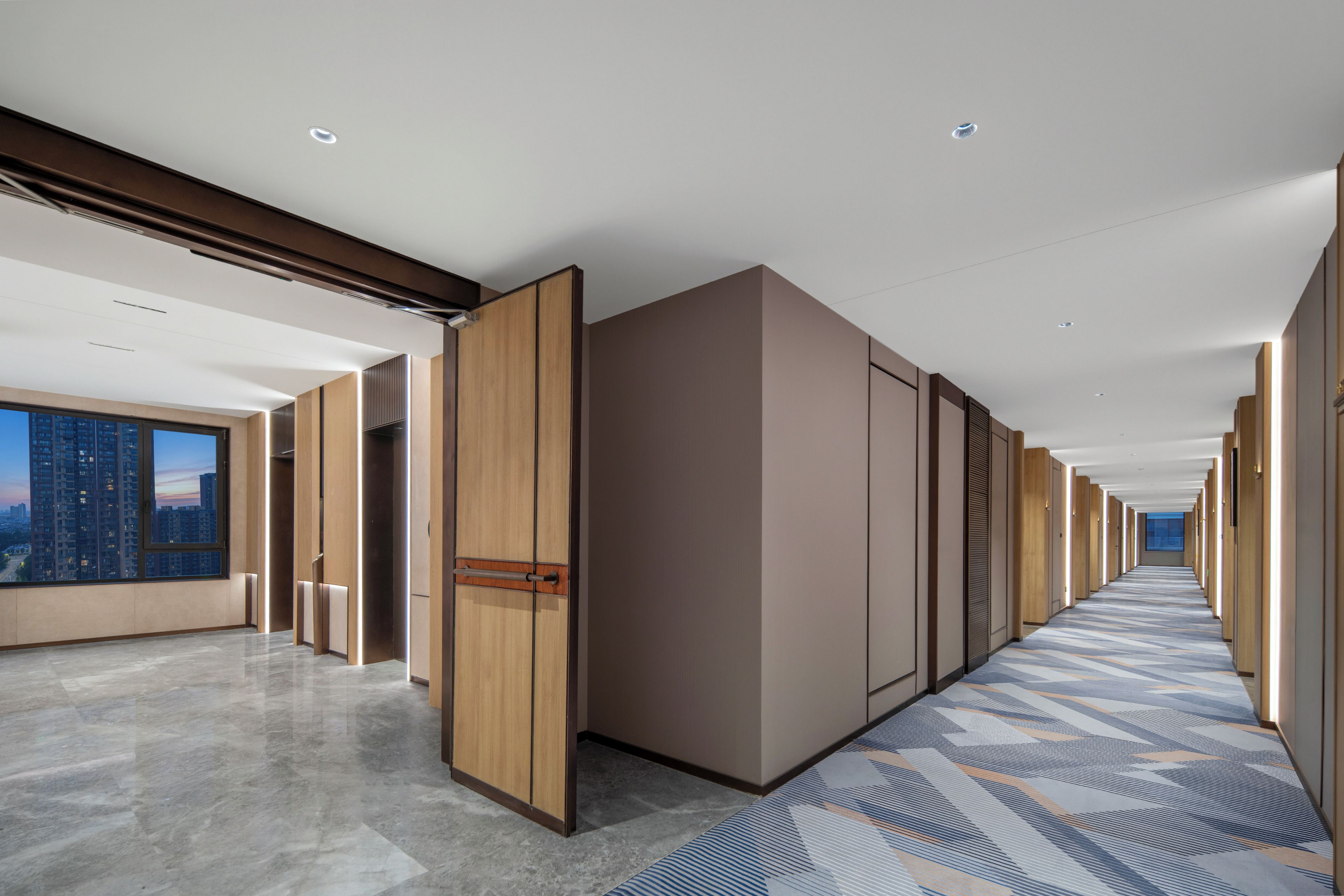 A modern hotel corridor with a long hallway, wooden doors, and a patterned carpet.