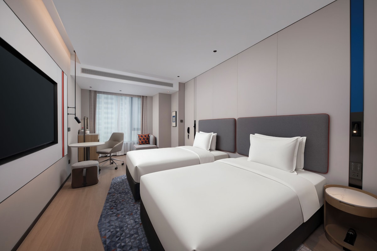 A hotel room with two beds, a desk, a chair, and a TV.