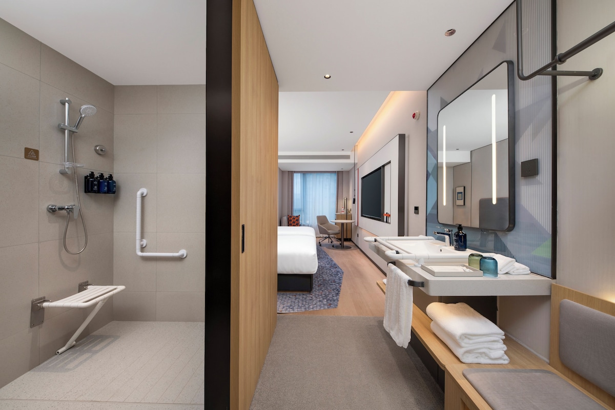 A modern hotel bathroom with a shower, toilet, and a vanity with a mirror.