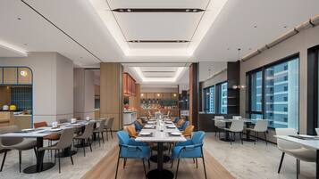 A modern dining area with long tables, chairs, and a kitchen in the background.