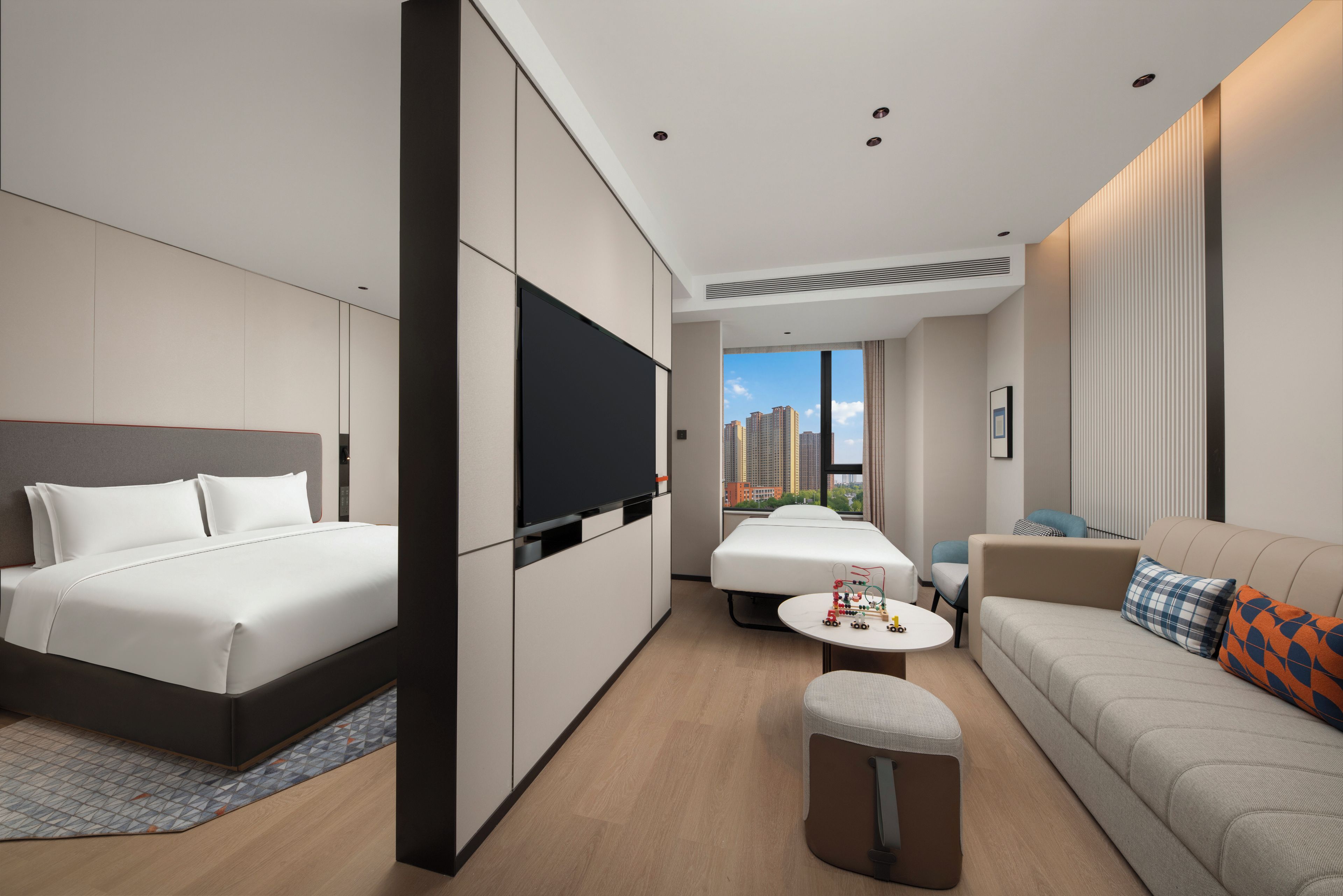 Una habitación de hotel moderna con una cama grande, un sofá, una mesita y un televisor.