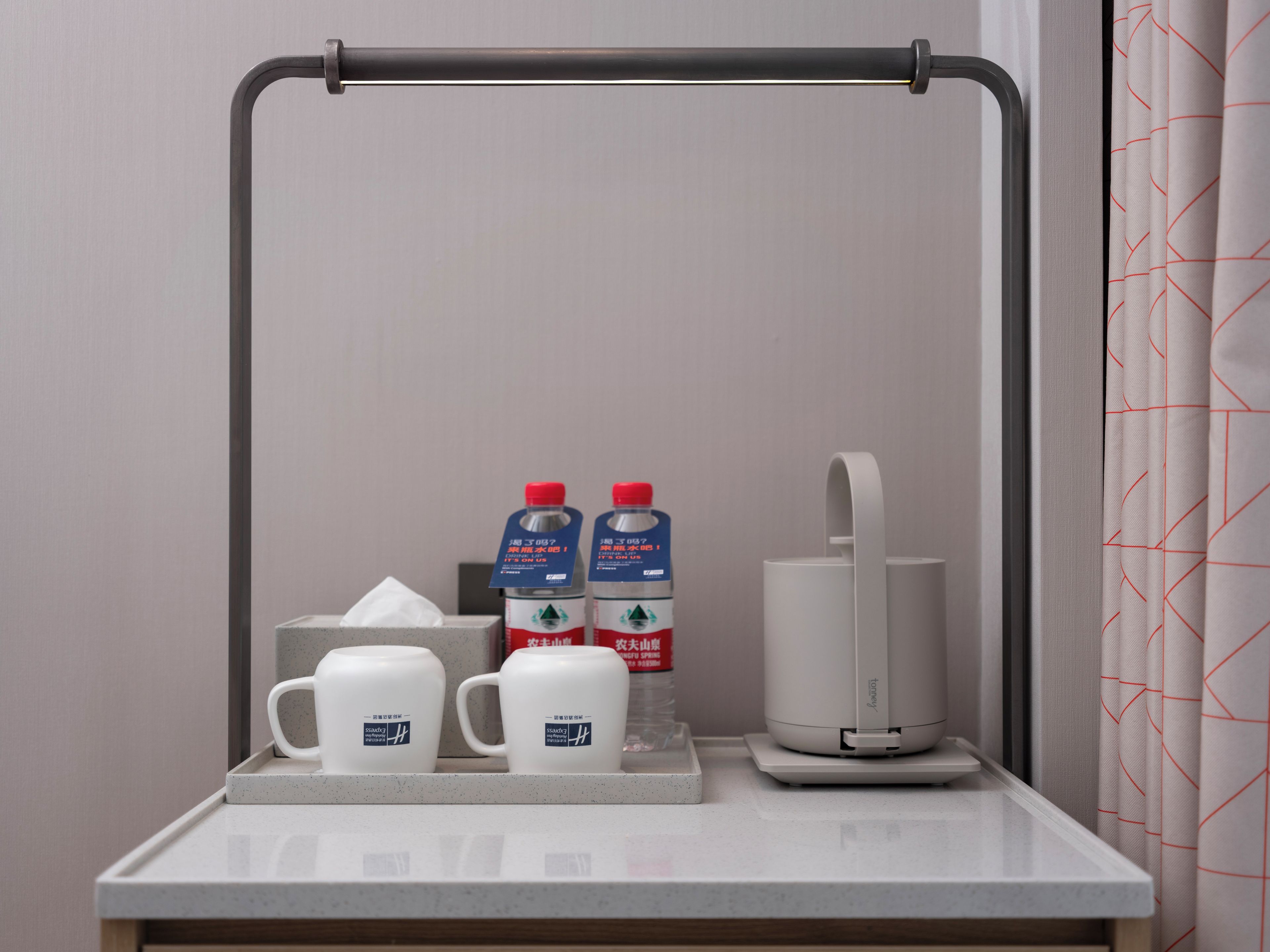 A bathroom counter with a towel dispenser, two bottles of water, and two white mugs.