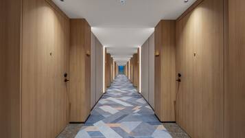 A hotel corridor with wooden doors, a patterned carpet, and a straight ceiling with recessed lighting.