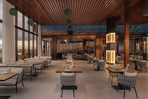A restaurant with multiple dining tables and chairs, large windows, and a ceiling with hanging spherical decorations.