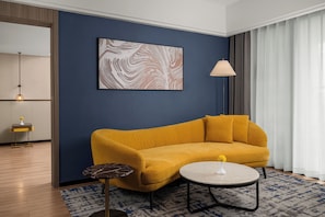 A modern living room with a blue accent wall, a mustard-colored sofa, a round coffee table, a floor lamp, and a minimalist side table.