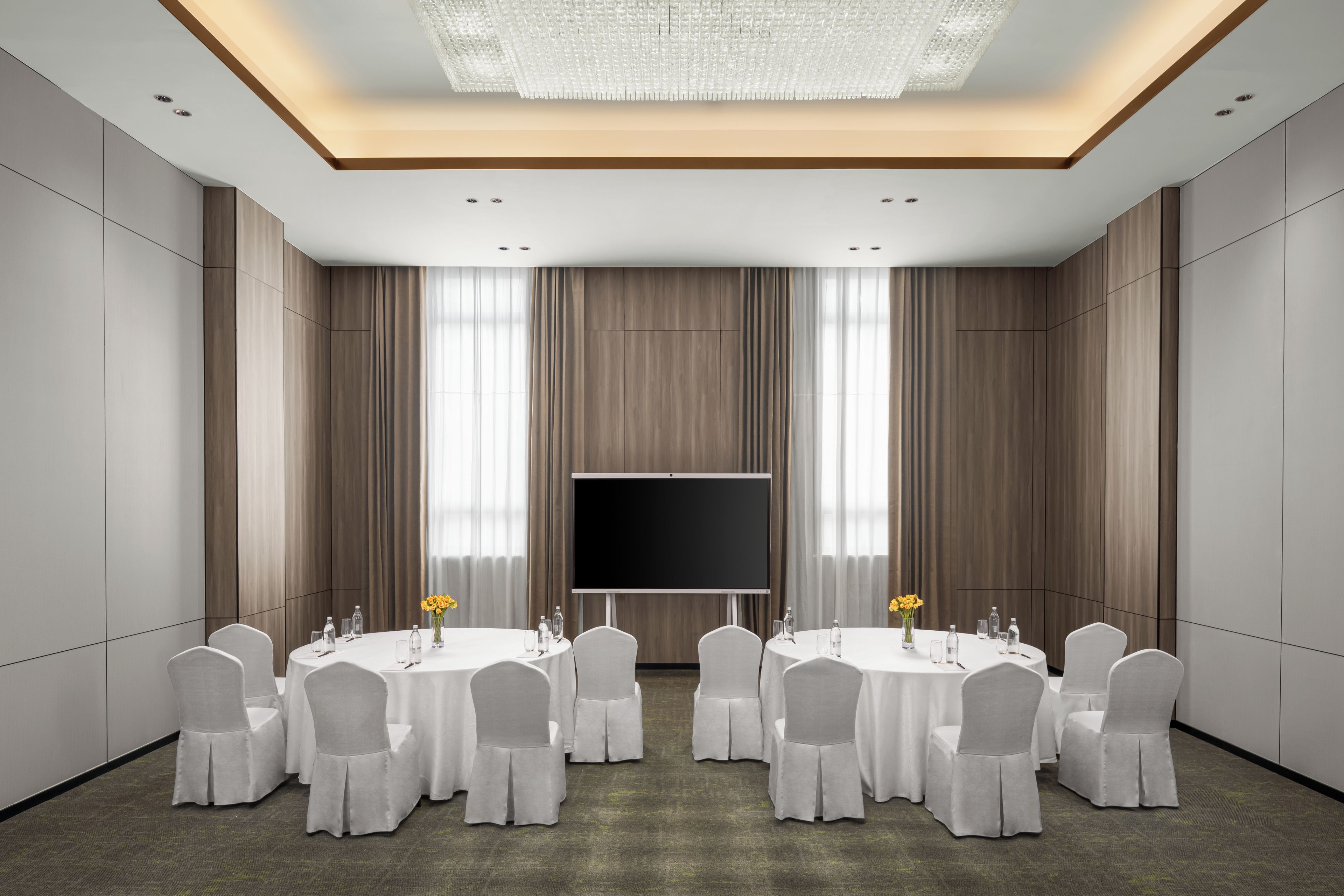 A conference room with a large flat-screen TV, round tables, and chairs.