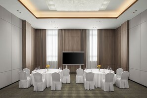 A conference room with a large flat-screen TV, round tables, and chairs.