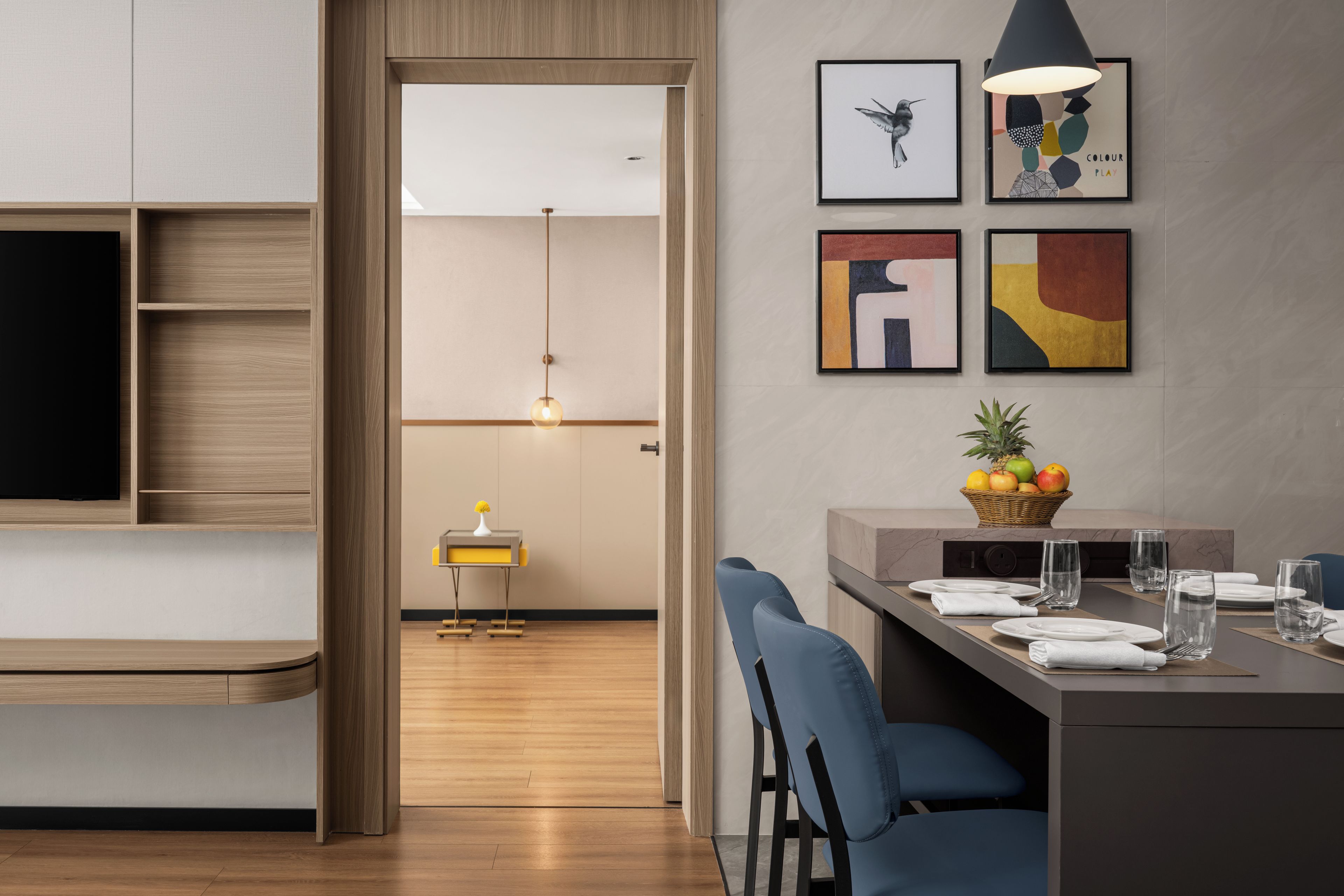 Una cocina moderna con comedor, armarios de madera, televisor y una cesta de fruta en la encimera.
