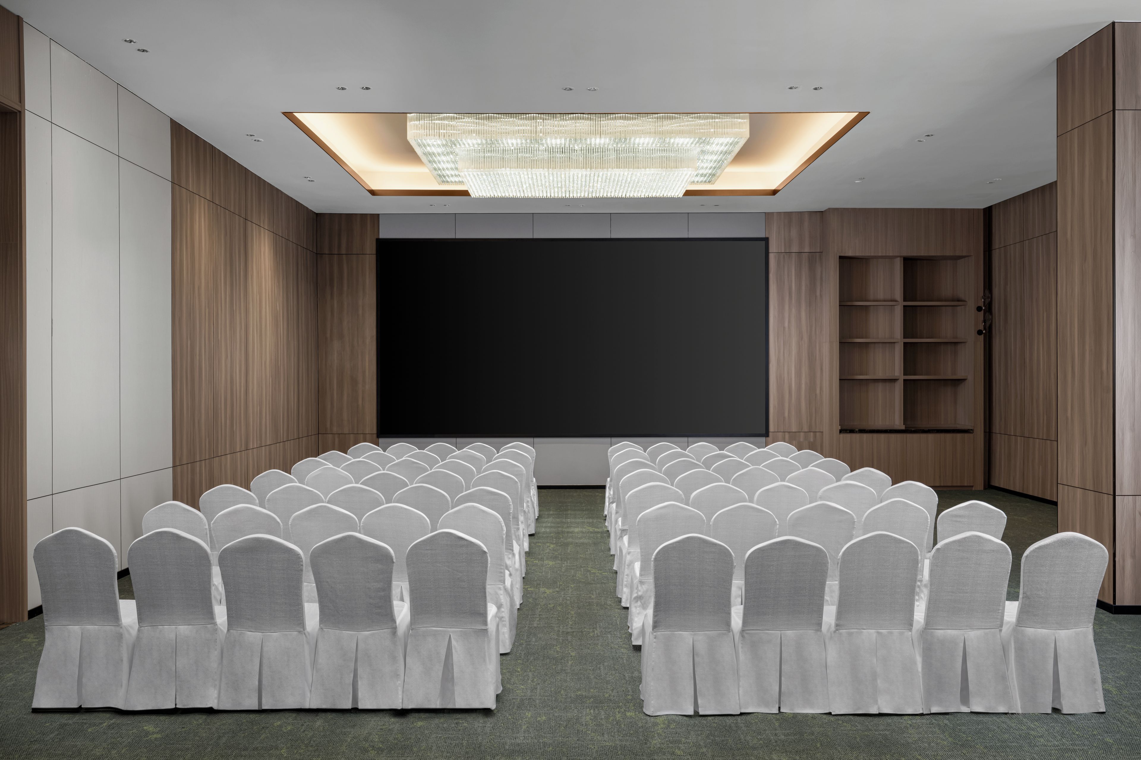 Un salón de conferencias con filas de sillas, una pantalla grande y una araña.