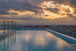 A rooftop pool with a view of the airport and mountains in the distance.