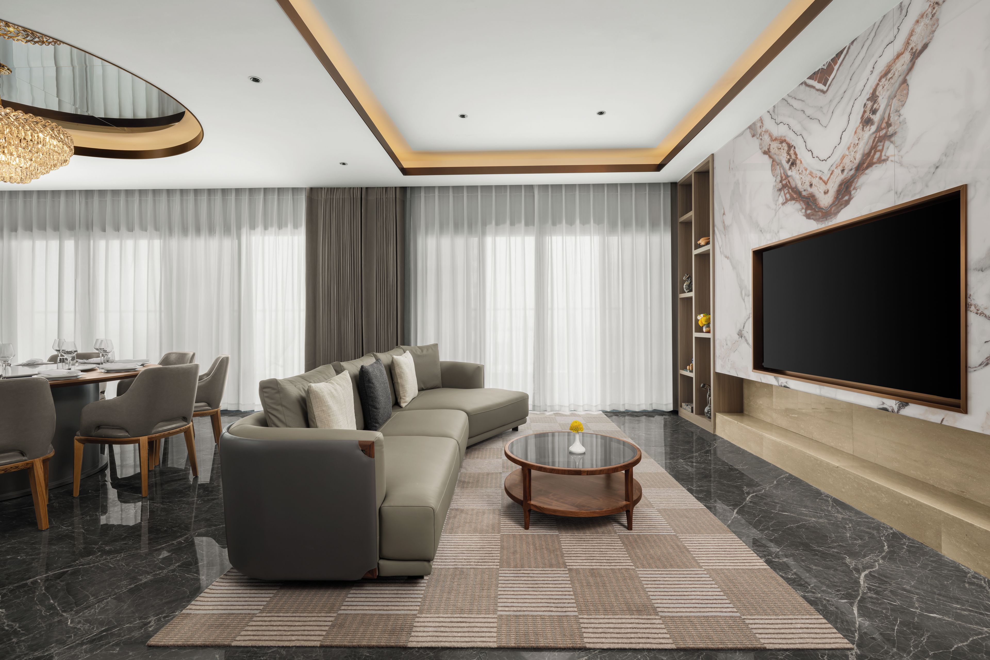 A modern living room with a sectional sofa, a round coffee table, and a large flat-screen TV mounted on the wall.
