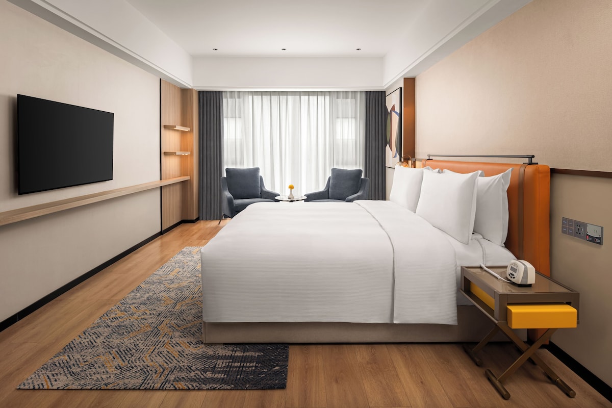A hotel room with a large bed, two chairs, a TV, and a bedside table with a phone.