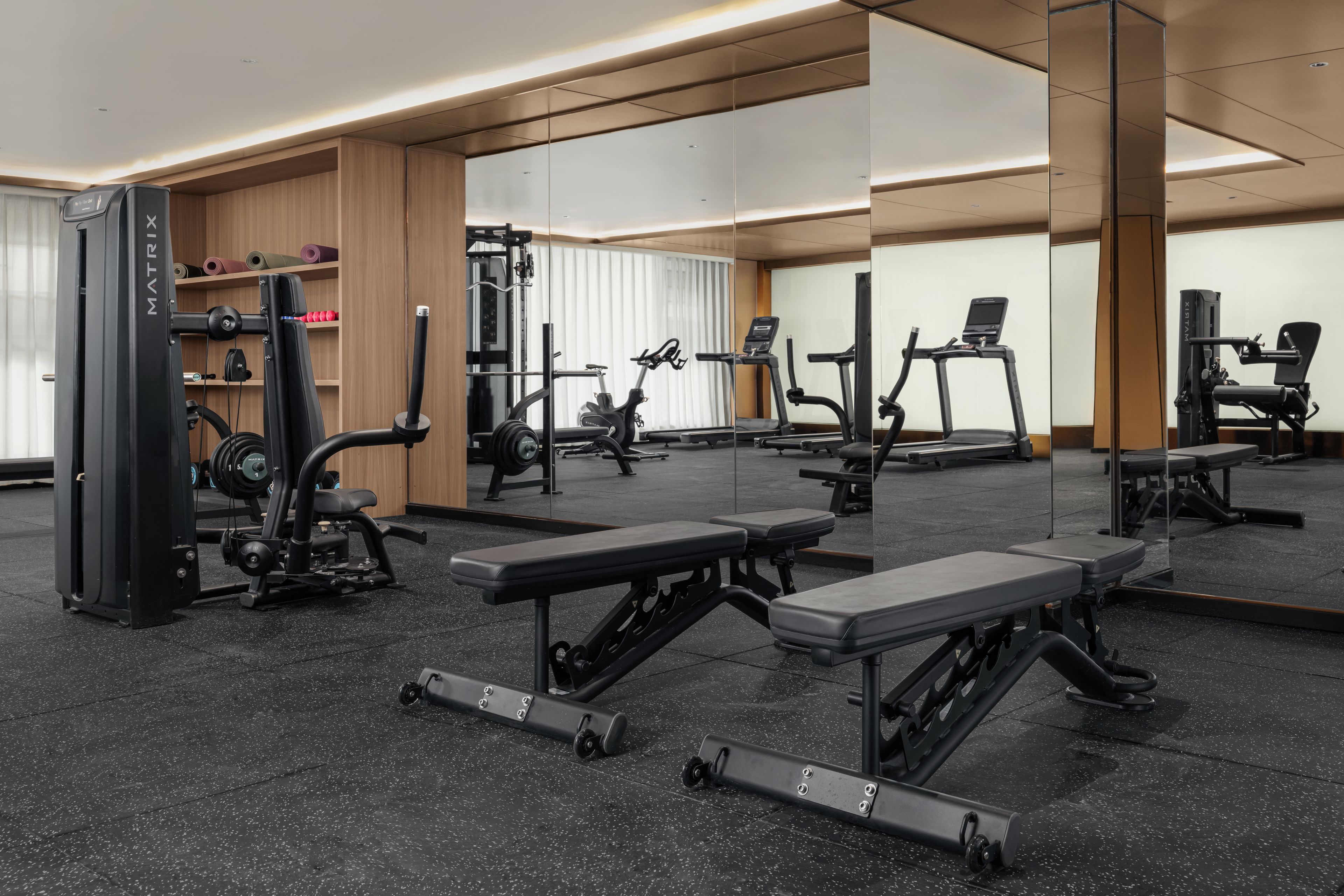 Un gimnasio con varios equipos de ejercicio, como cintas de correr, máquinas de pesas y bancos.