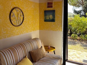 A room with a sofa, a small round table, and a view of greenery outside. - La Quercia Two-Room Apartment in the Heart of the Maremma (Grosseto)