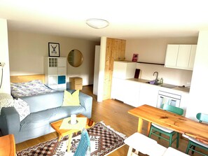 Un espacio habitable compacto con kitchenette, comedor y sofá con una manta estampada.