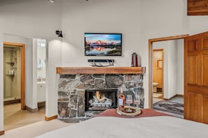 A bedroom with a stone fireplace, a mounted TV, and a bed with a red throw. - Abode at Winterhaven, hot tub pool, Deer Valley (Park City)
